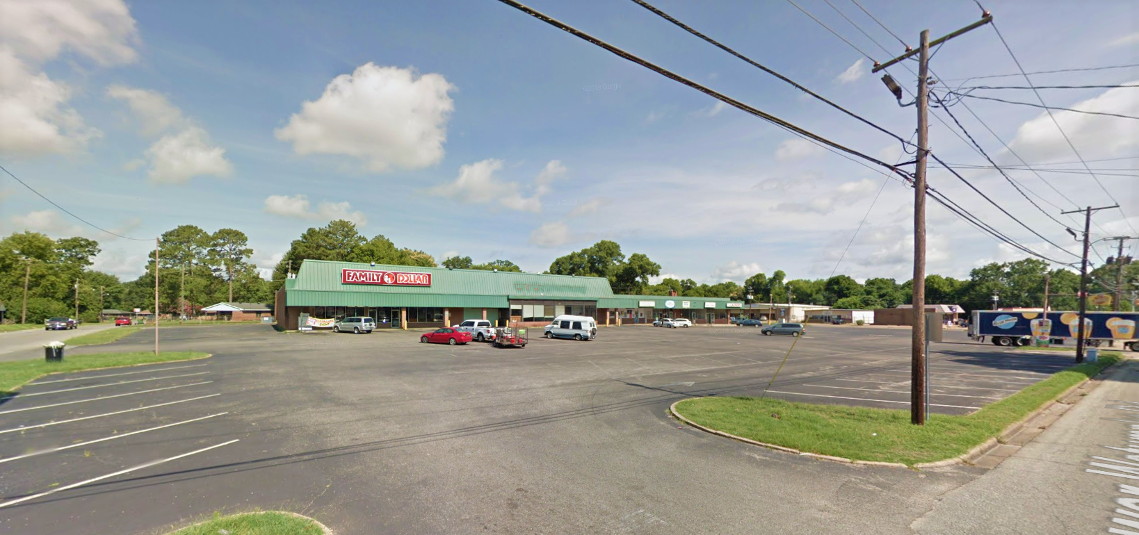 Suburban strip mall with Family Dollar, parking lot, and nearby trees on a sunny day.